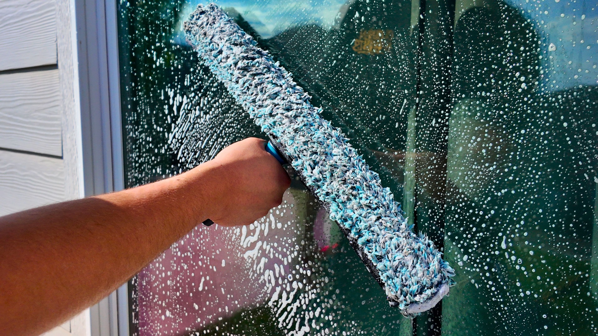 Microfiber T-bar scrubbing soap across a large exterior window